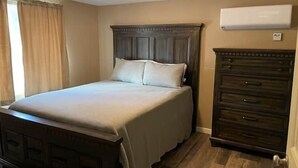 A bedroom with a bed, wooden dresser, and an air conditioning unit.