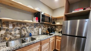 A kitchen with granite countertops, wooden cabinets, a stainless steel refrigerator, a microwave, and a stone backsplash. - Elk Haven Cabins - Cabin 4 (Payson)