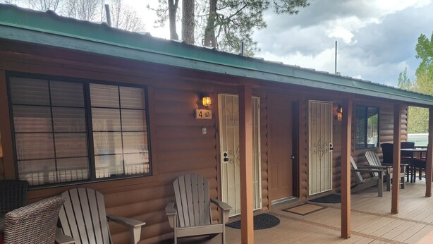 A cabin with a wooden deck, two Adirondack chairs, a wicker chair, and a covered porch area. - Elk Haven Cabins - Cabin 4 (Payson)
