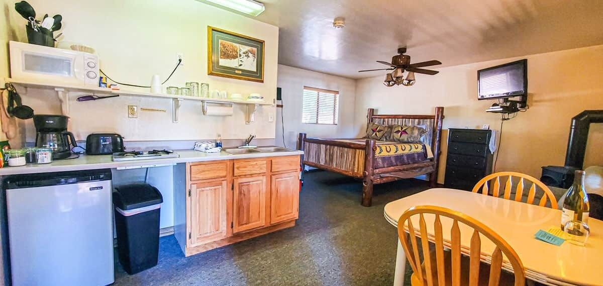 A compact kitchen with a microwave, coffee maker, and sink. There is a wooden dining table with chairs and a ceiling fan.