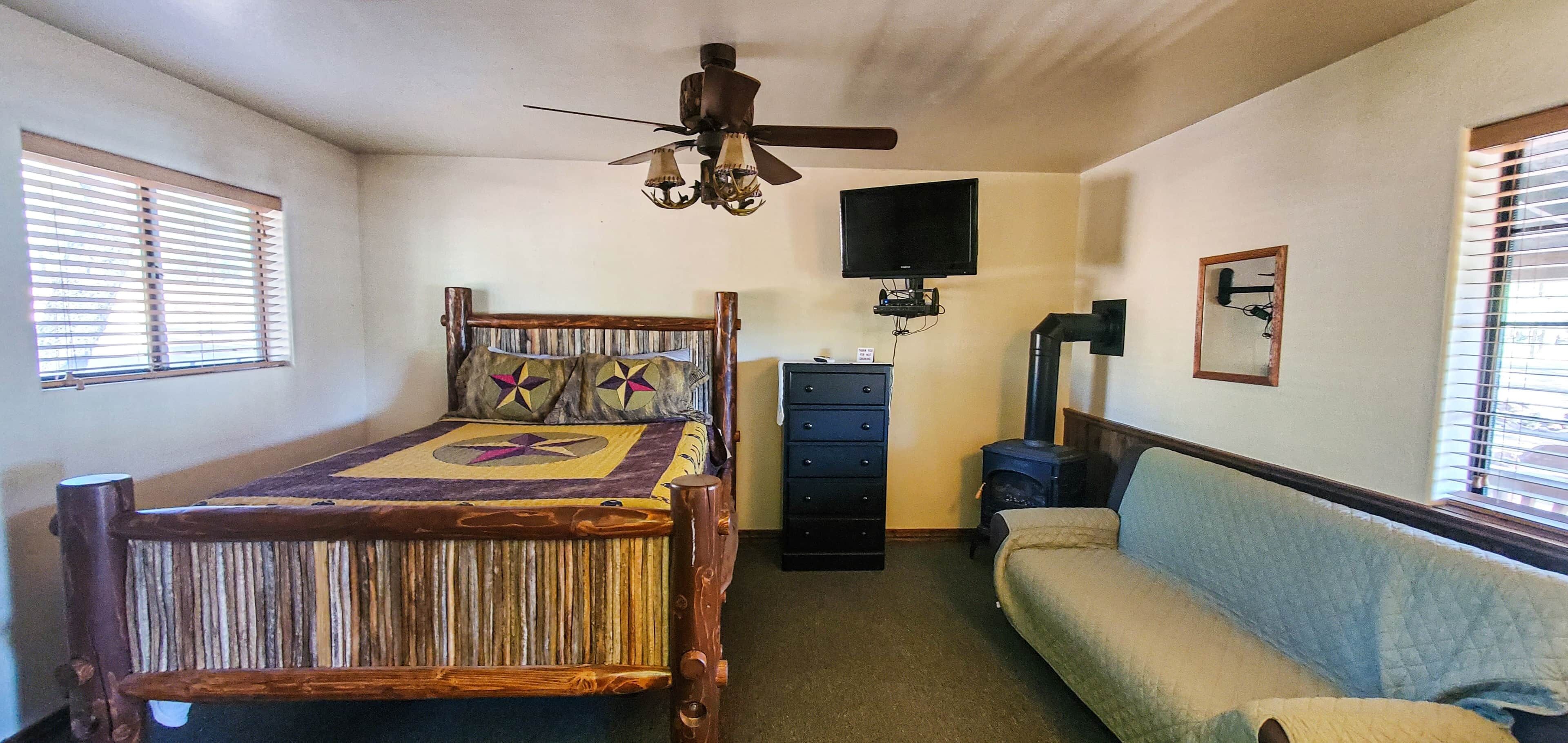 A bedroom with a wooden bed, a dresser, a television, a heater, and a window with blinds.