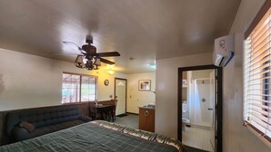 A bedroom with a bed, a ceiling fan, a dining table with chairs, a bathroom with a toilet, and a window with blinds. - Elk Haven Cabins - Cabin 2 (Payson)