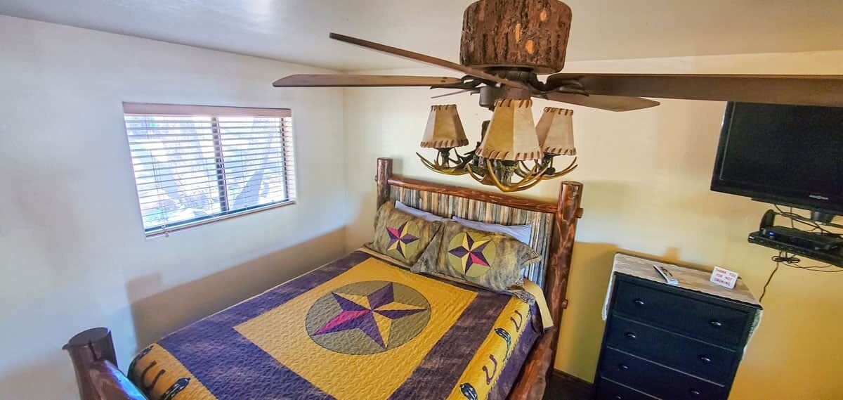 A bedroom with a bed, a ceiling fan, a TV, and a dresser.