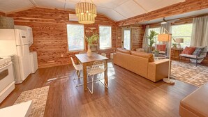 A cozy cabin interior with a wooden interior, a dining area with a table and chairs, a sofa, and a kitchen with a refrigerator and stove. - Skip Rock Cottage ~ ON Livingston Creek (Mountain View)