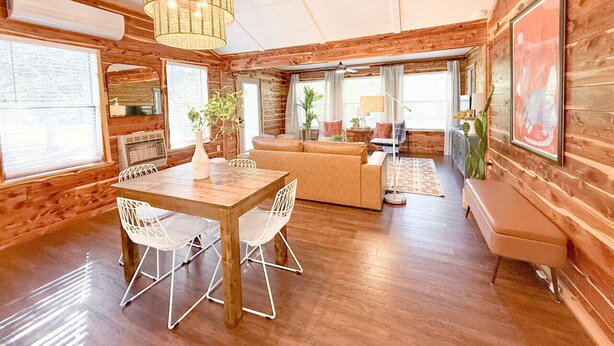 A spacious room with a wooden interior, a dining table with chairs, a sofa, a bench, and a hanging light fixture. - Skip Rock Cottage ~ ON Livingston Creek (Mountain View)