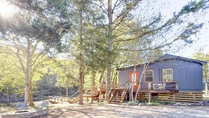 A rustic cabin with a wooden deck, surrounded by trees. - Skip Rock Cottage ~ ON Livingston Creek (Mountain View)