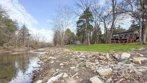 A riverside property with a wooden cabin, a rocky shoreline, and a forested area. - Skip Rock Cottage ~ ON Livingston Creek (Mountain View)