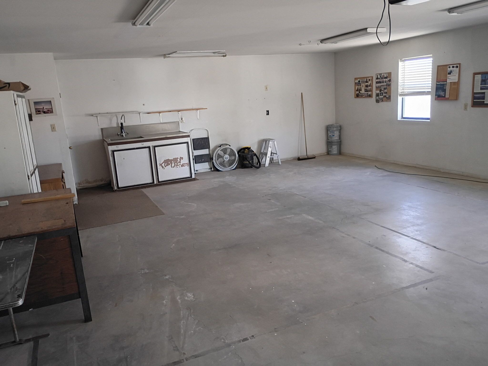 A spacious room with a kitchenette, a large window, and a concrete floor.