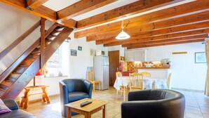 A spacious living area with a wooden staircase, a dining table with chairs, and a kitchen in the background.