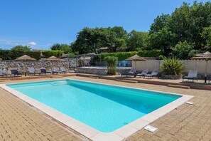 A rectangular swimming pool with a tiled edge, surrounded by lounge chairs and umbrellas, with a stone wall and greenery in the background.