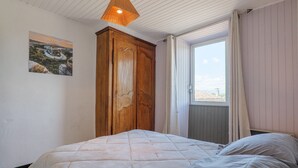 Een slaapkamer met een bed, een houten kledingkast, een raam met gordijnen en een schilderij aan de muur.