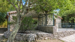 Un bâtiment en pierre avec un toit en tuiles, une clôture en métal et un arbre devant.