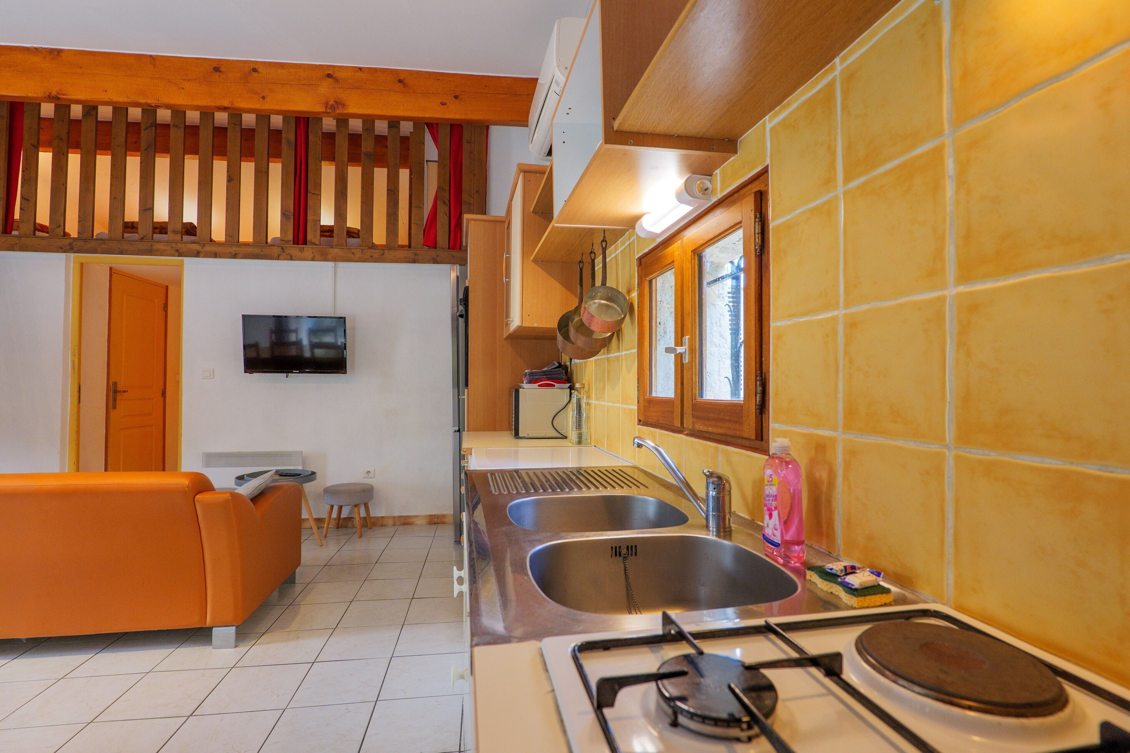 Una cocina con estufa a gas, dos fregaderos, techo de madera y un televisor montado en la pared.