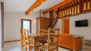 Un espace repas comprenant une table et des chaises en bois, un canapé, un escalier et un téléviseur fixé au mur.
