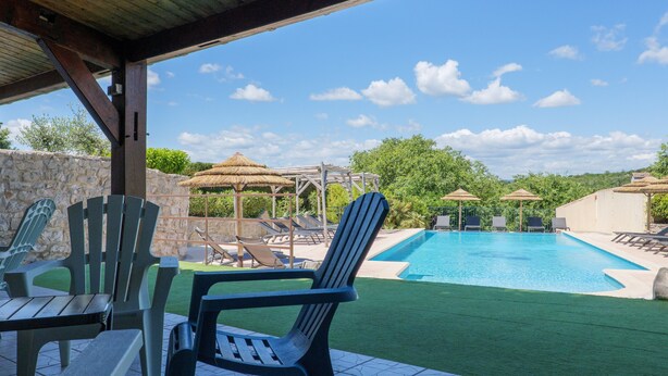 Un espace piscine avec des chaises et des parasols, un mur en pierre et un ciel dégagé.