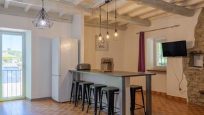 Een keuken met een bar, krukken, een koelkast, hangende lampen en een stenen muur.