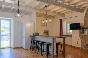 A kitchen with a bar area, stools, a refrigerator, hanging lights, and a stone wall.