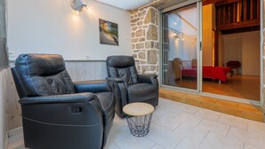 A room with two reclining chairs, a small round table, a stone wall, and a sliding glass door leading to another room.