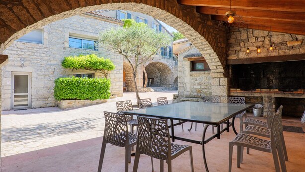 An outdoor patio with a glass table and metal chairs, stone walls, and a stone fireplace.
