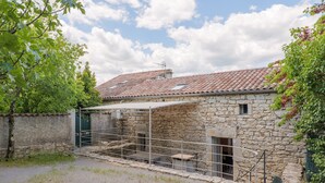 Un bâtiment en pierre avec un toit en tuiles, un portail en métal et une petite fenêtre.