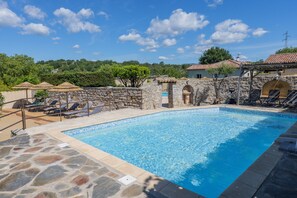 A swimming pool with stone walls, lounge chairs, and umbrellas.