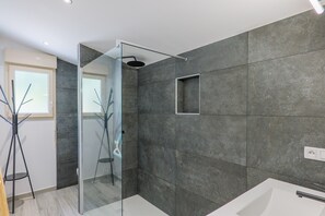 Un baño moderno con cabina de ducha de vidrio, una bañera blanca y un espejo grande.