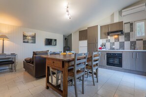 A modern kitchen with a dining area, wooden cabinets, a built-in oven, and a flat-screen TV.