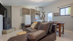 Eine moderne Küche mit Einbauherd, ein Essbereich mit Holztisch und Stühlen sowie ein Wohnbereich mit Sofa und Kissen.