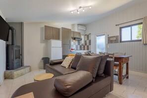 Una cocina moderna con estufa integrada, un comedor con mesa y sillas de madera, y una sala de estar con sofá y cojines.
