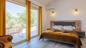 Ein Schlafzimmer mit Bett, Nachttisch, Sessel und Blick ins Freie.