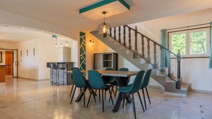 Un grand espace à manger avec une table et des chaises, une cuisine en arrière-plan et un escalier avec une rampe.