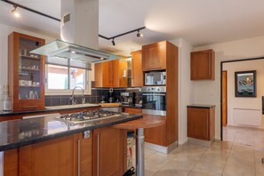 Een moderne keuken met een centraal eiland, roestvrijstalen apparatuur, houten kastjes en een glazen afzuigkap.