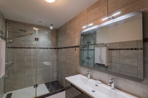 Een moderne badkamer met een glazen douchecabine, een grote spiegel en een wit wastafelmeubel.