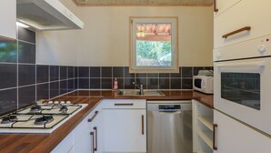 Cocina con estufa a gas, microondas, lavavajillas y ventana con vistas al verdor.