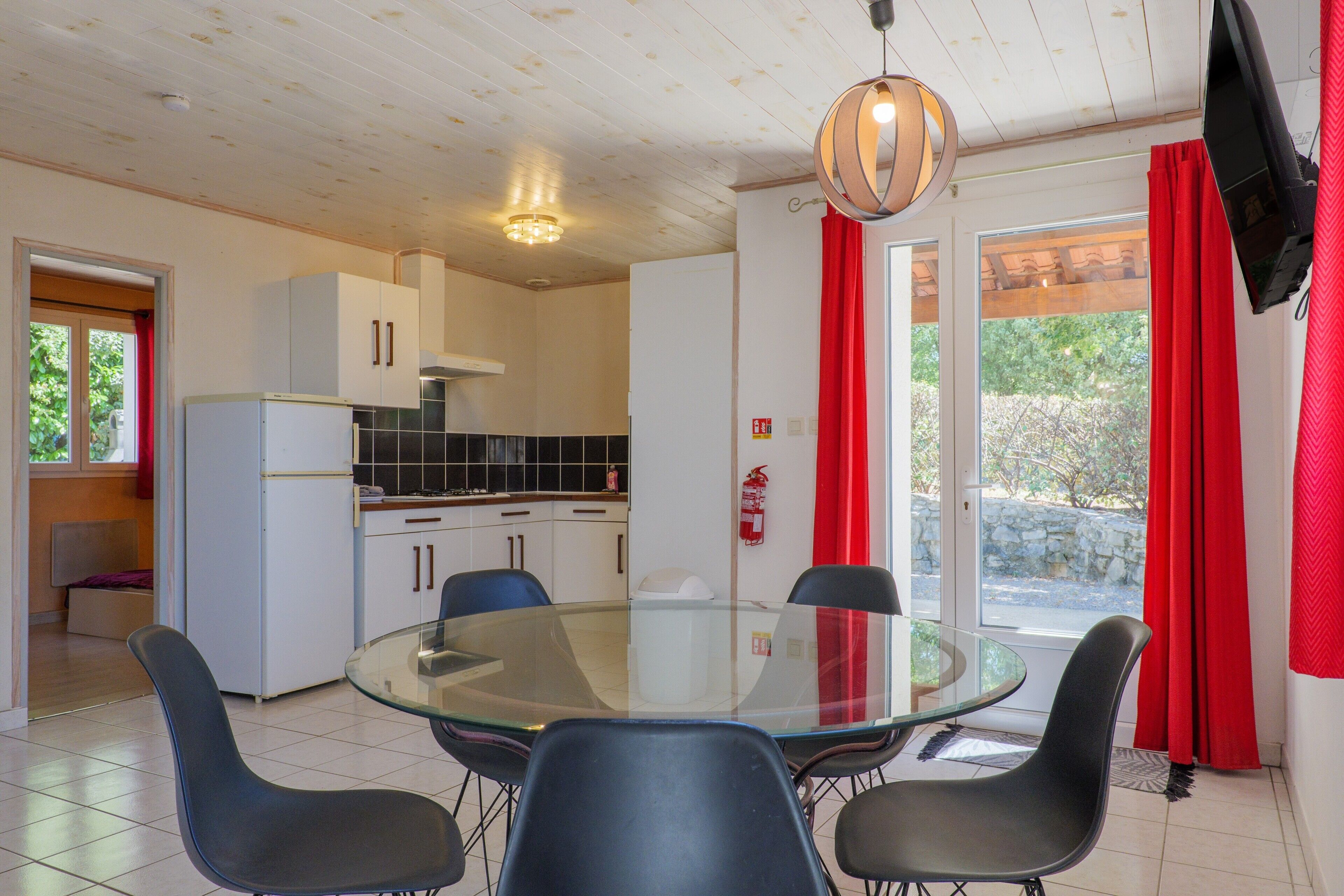Une cuisine de taille réduite avec des meubles blancs, un réfrigérateur et une table à manger en verre entourée de chaises.