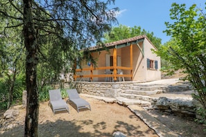Una casa de piedra con balcón, dos sillones de descanso y un muro de piedra.