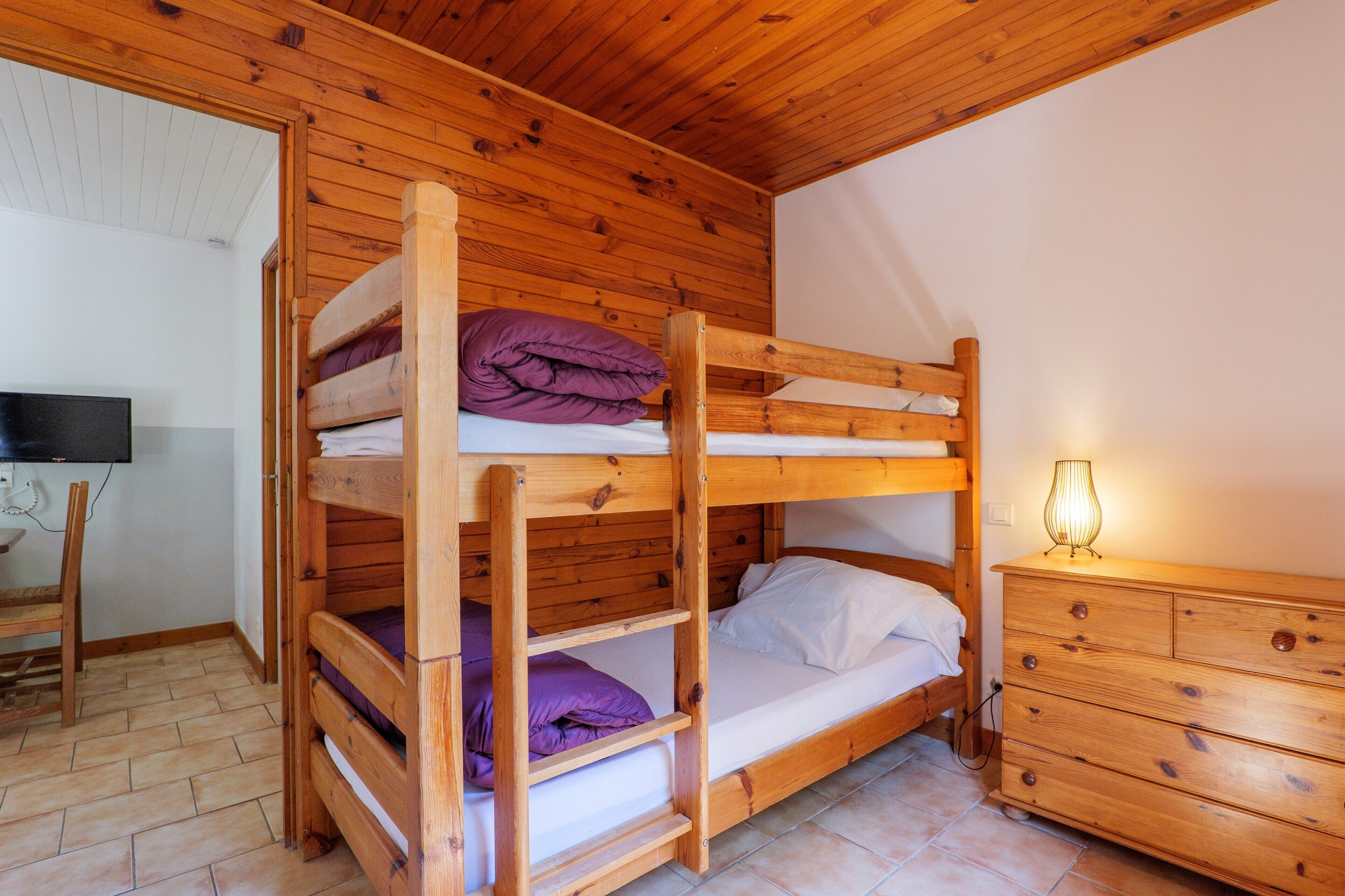 Habitación con literas, paredes de madera, televisor, cómoda y lámpara.