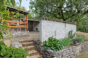 A rustic outdoor seating area with stone steps, a wooden pergola, and lush greenery.