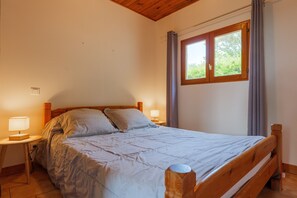 Une chambre Ă coucher avec un lit en bois, deux tables de chevet avec des lampes, une fenĂȘtre avec des rideaux et un plafond en bois.