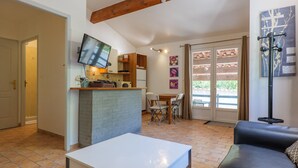 Un salon avec une table blanche, un canapé en cuir noir, un téléviseur fixé au mur et un coin repas comprenant des chaises et une table.