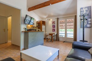 Un salon avec une table blanche, un canapé en cuir noir, un téléviseur fixé au mur et un coin repas comprenant des chaises et une table.
