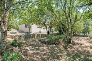 Un bâtiment aux murs de pierre, à l’extérieur blanc, entouré d’arbres et de verdure.