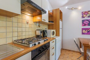 A compact kitchen with a gas stove, oven, coffee maker, and a microwave. - Gîte Noisetier – Village of Holiday Cottages (Joyeuse)