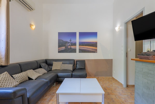 Una sala de estar con un sofá de cuero negro, almohadones estampados, una mesa de centro blanca y dos cuadros colgados que muestran un paisaje.