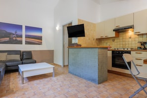 Un espacio habitable compacto con sofá, mesa de centro, cocina con estufa y televisor montado en la pared.
