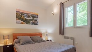 Une chambre à coucher comprenant un lit, deux tables de chevet avec des lampes, un radiateur fixé au mur et une fenêtre avec des rideaux.