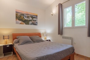 Une chambre à coucher comprenant un lit, deux tables de chevet avec des lampes, un radiateur fixé au mur et une fenêtre avec des rideaux.