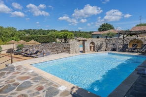 Una piscina con paredes de piedra, sillas de descanso y sombrillas.