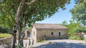 Un bâtiment en pierre, doté d’un toit en tuiles, entouré de gravier et de verdure.