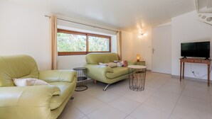 Un salon avec deux canapés, une petite table ronde, un téléviseur posé sur un meuble en bois et une fenêtre avec des rideaux.